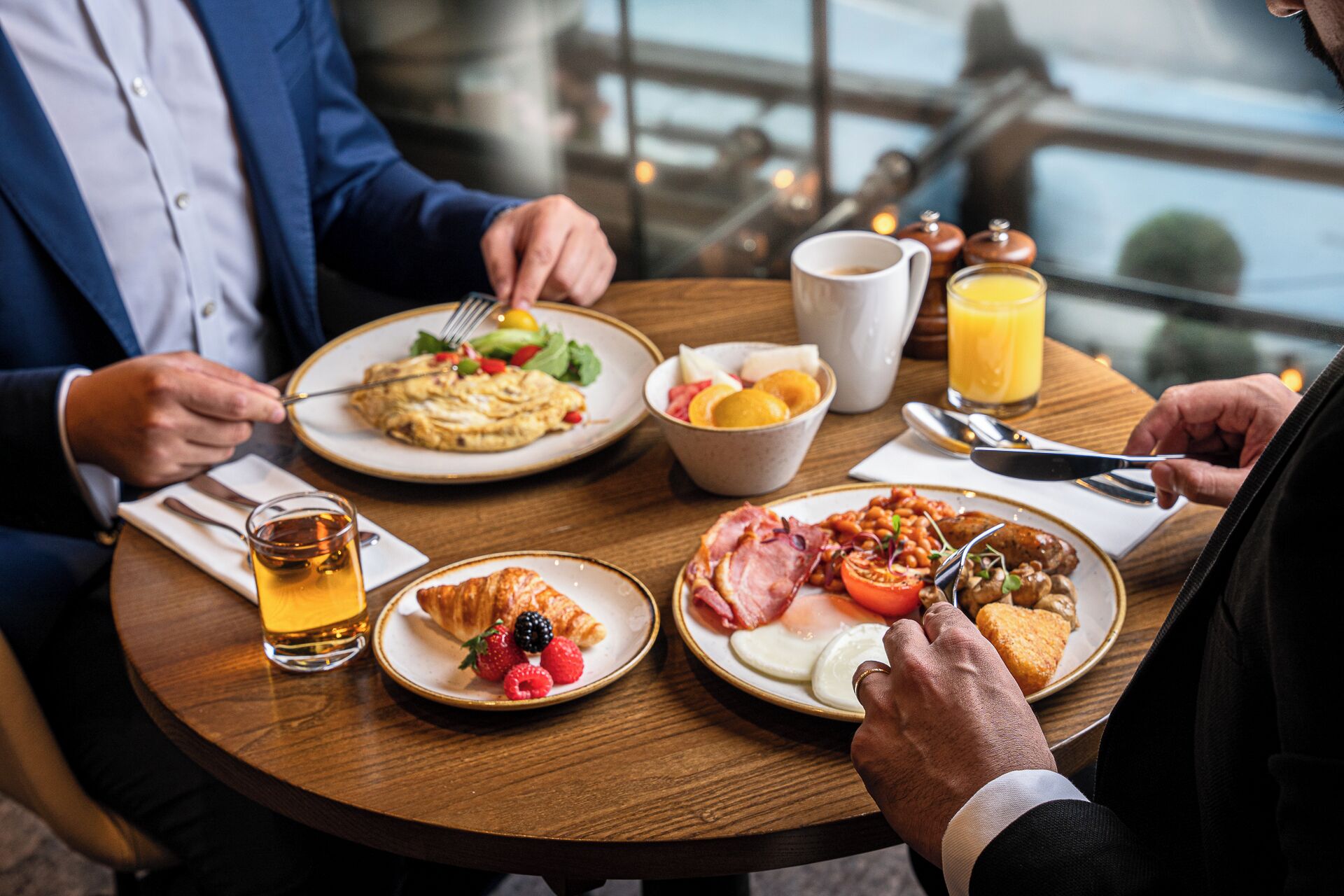 A breakfast setting with plates of food, a glass of juice, and a cup of tea.