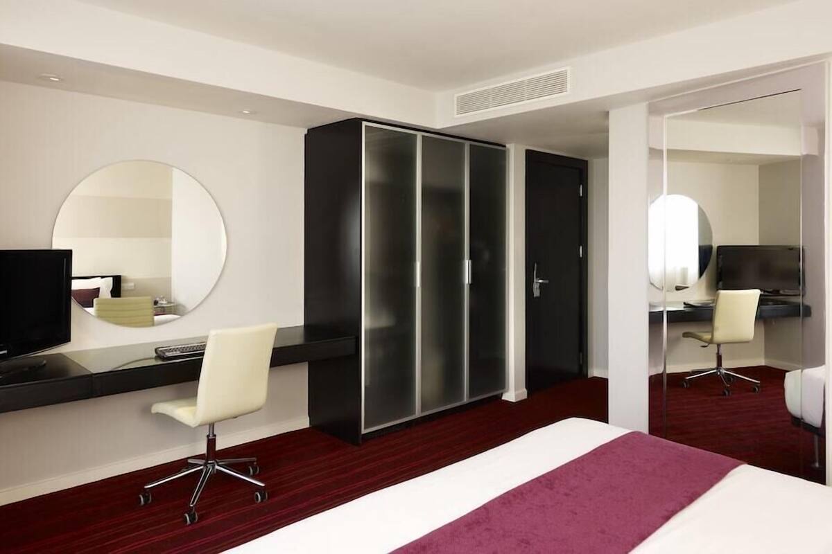 A hotel room with a bed, a desk with a chair, a television, and a wardrobe.