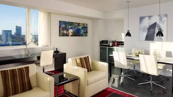 A modern hotel room with a city view, a dining area, and a living space with a sofa and chairs.