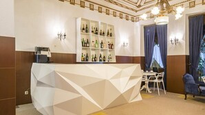 A bar area with a geometric white counter, shelves with bottles, and a seating area with chairs and a sofa. - Costa do Sol Residencial (Porto)