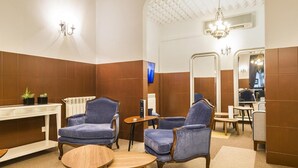 A bathroom with two blue armchairs, a wooden table, a mirror, and a chandelier. - Costa do Sol Residencial (Porto)