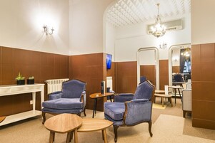 Casa de banho com duas poltronas azuis, uma mesa de madeira, um espelho e um candeeiro.