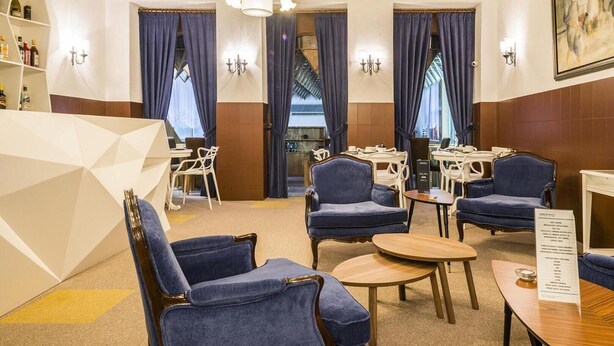 A hotel lobby with blue upholstered chairs, a chandelier, and a bar area with white chairs and tables. - Costa do Sol Residencial (Porto)