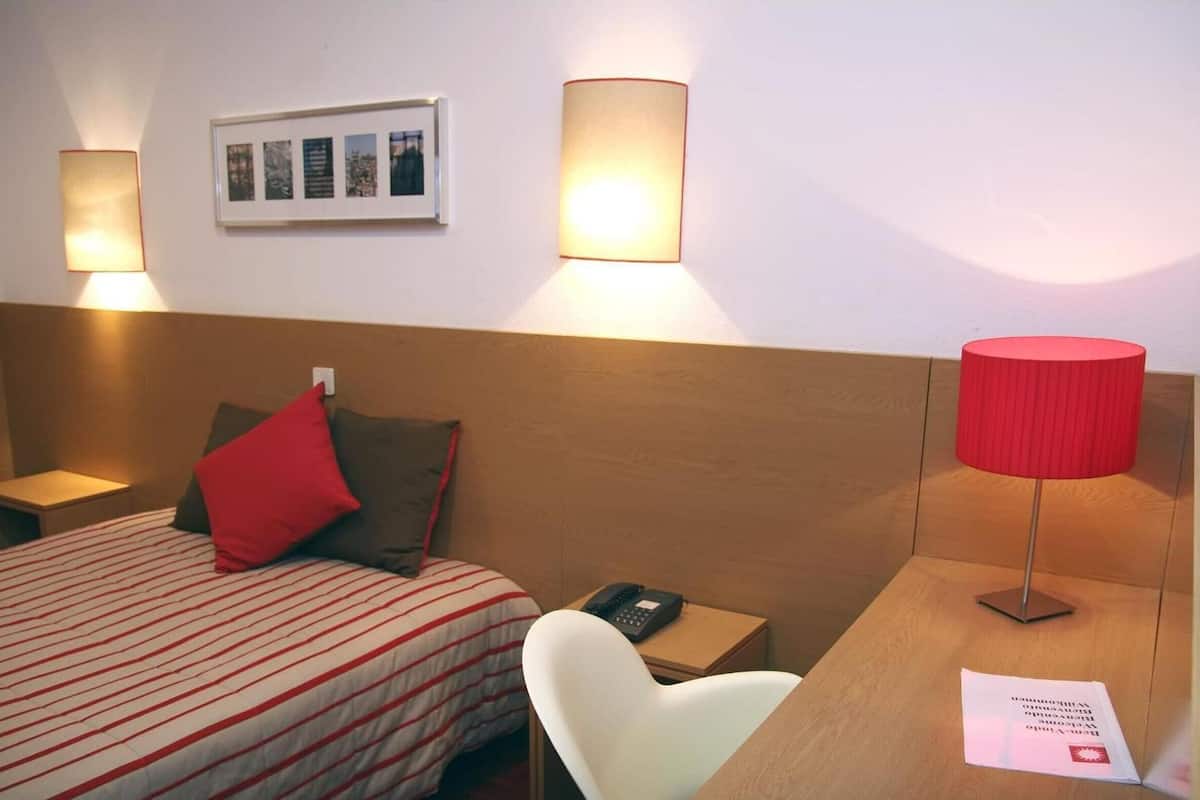 A hotel room with a bed, a desk, a chair, a phone, and two wall-mounted lamps.