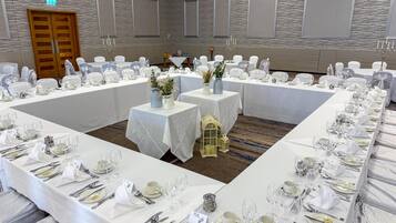A banquet hall with long tables set for a formal event, featuring white tablecloths, silverware, and glassware.