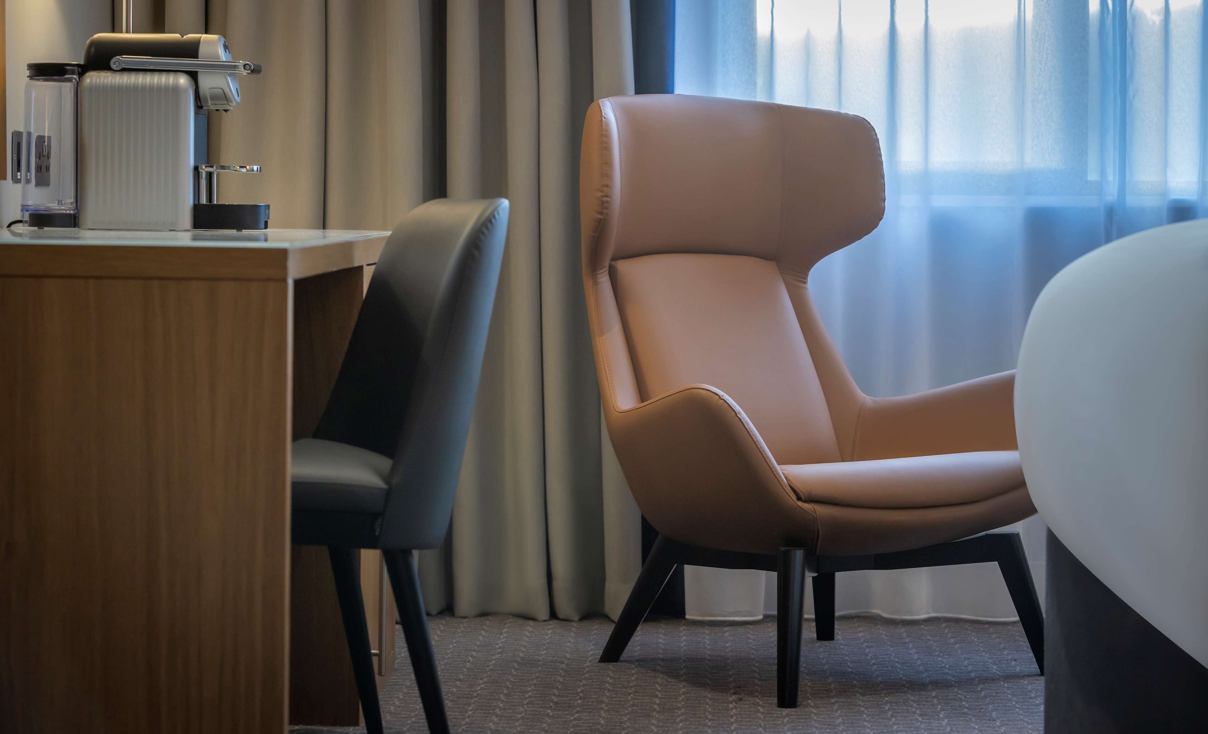 Een moderne hotelkamer met een houten bureau, een leren fauteuil en een groot bed.