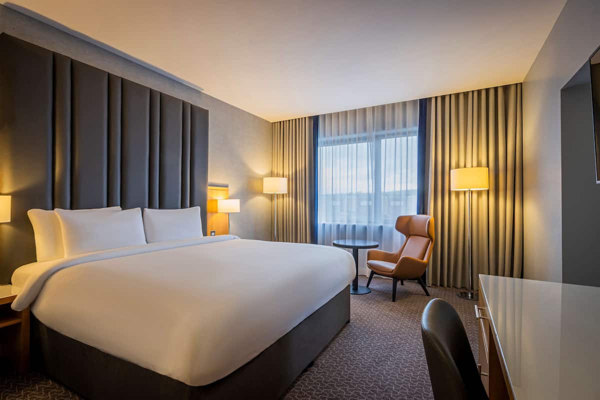 A hotel room with a large bed, a desk, a chair, and a window with curtains.