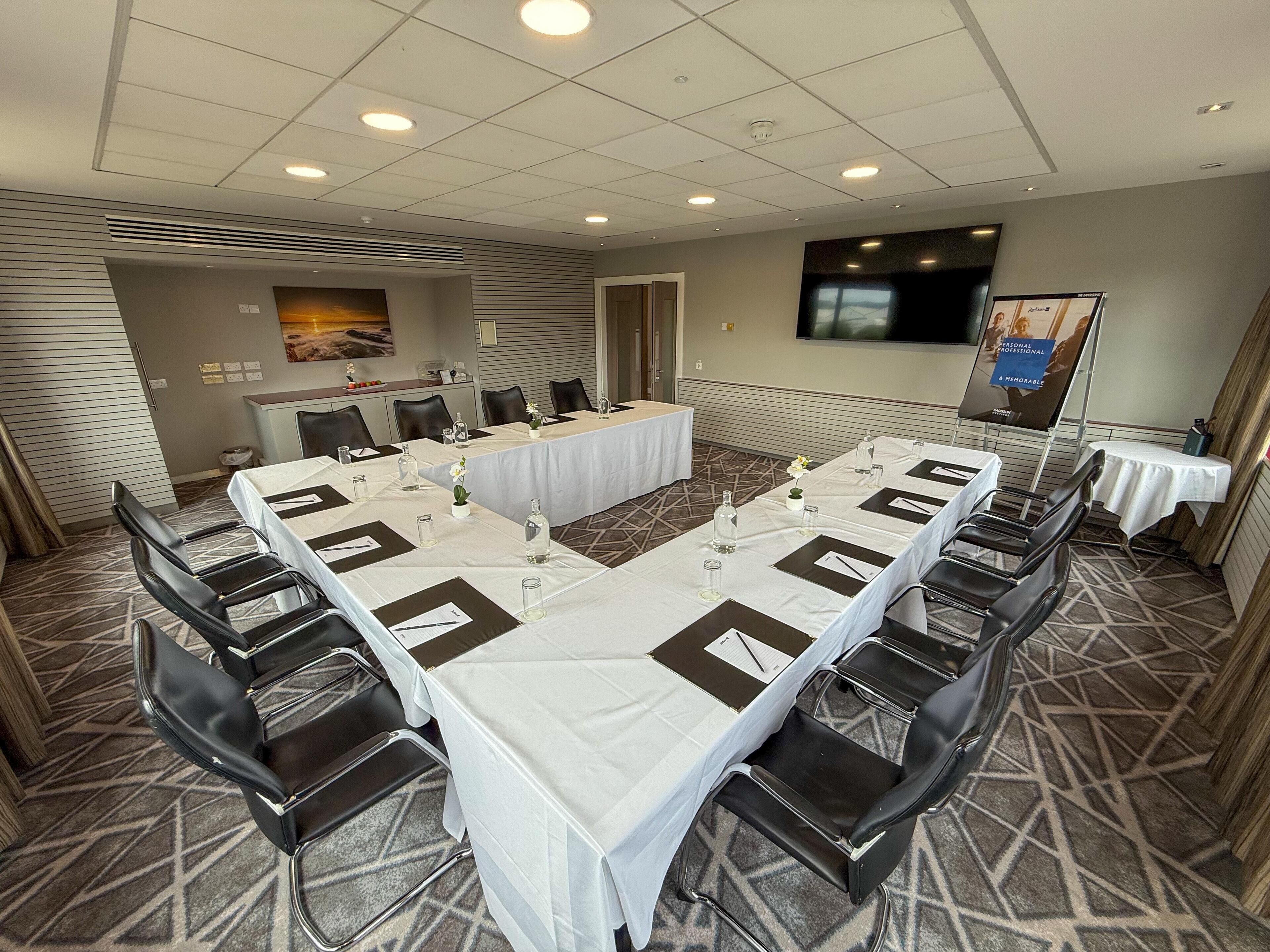 Une salle de conférence avec une longue table, des chaises et un écran de télévision.