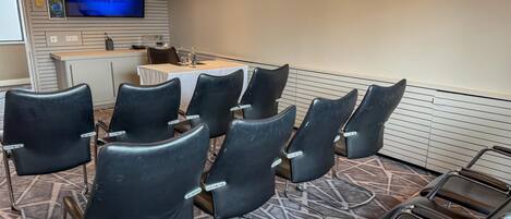 A conference room with black chairs, a table, a TV screen, and a reception desk.