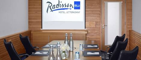 Un salón de conferencias con pared de paneles de madera, el logotipo de Radisson BLU y una pantalla de proyector.