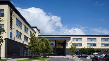 A modern building with a flat roof, large windows, and a parking lot with several cars.