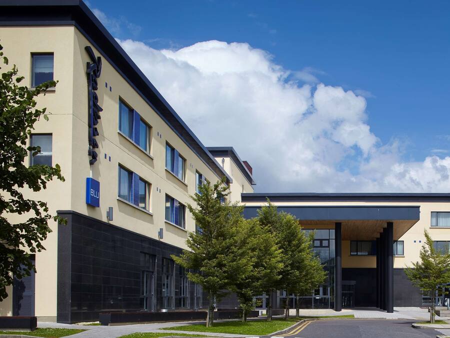 A modern building with a flat roof, large windows, and a parking lot with several cars.