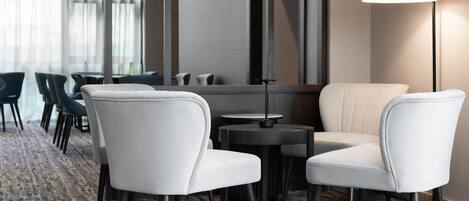 Un vestíbulo de hotel moderno con una alfombra estampada, sillas de cuero blanco, una mesa redonda y una lámpara de pie.