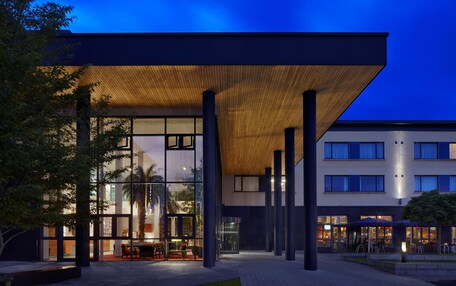 A modern building with a glass facade, outdoor seating area, and a covered patio.