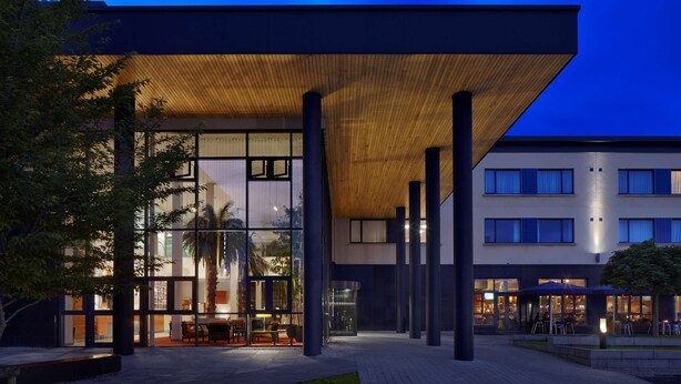 A modern building with a glass facade, outdoor seating area, and a covered patio.