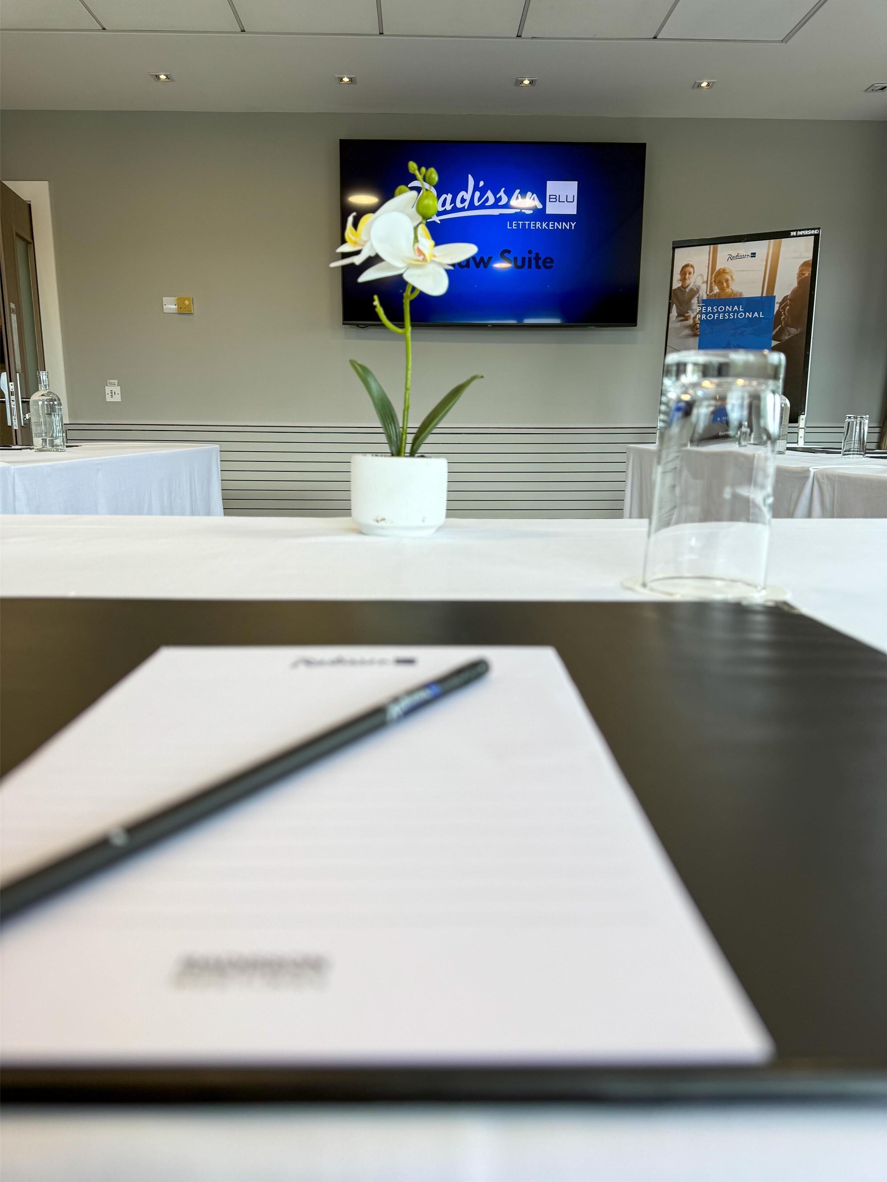 A conference room with a white table, a potted plant, a glass of water, and a document with a pen.