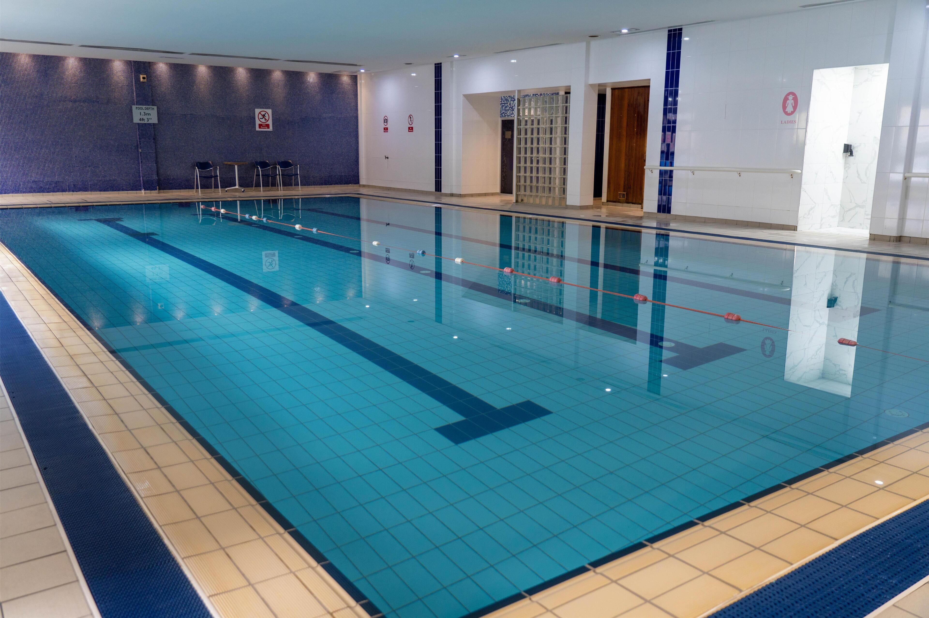 A large indoor swimming pool with clear lane markings, a tiled floor, and a blue-tiled wall.