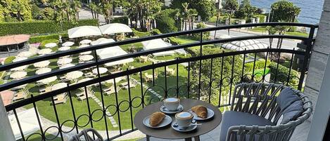 A balcony with two wicker chairs, a small table, and a view of a lake and mountains.