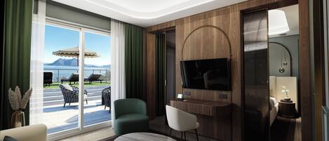 Habitación de hotel con un amplio ventanal corredero a un balcón, un televisor de pantalla plana montado en una pared de paneles de madera, una mesa redonda de mármol y una zona de estar con sofá y sillones.