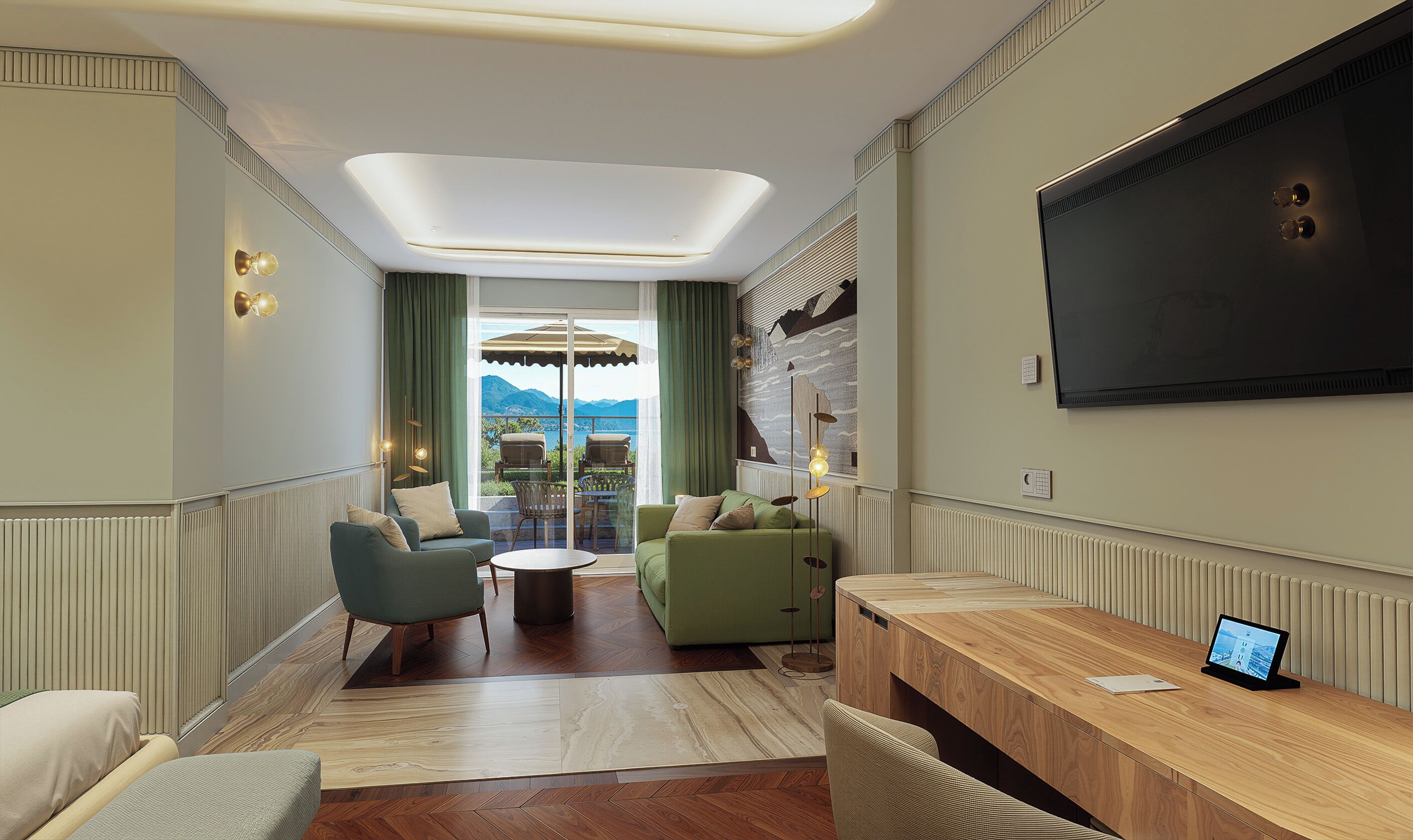 A modern hotel room with a large TV, a wooden desk, a green sofa, and a view of mountains.