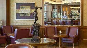 A bar area with leather chairs, a statue, and a large window with a view of the bar.