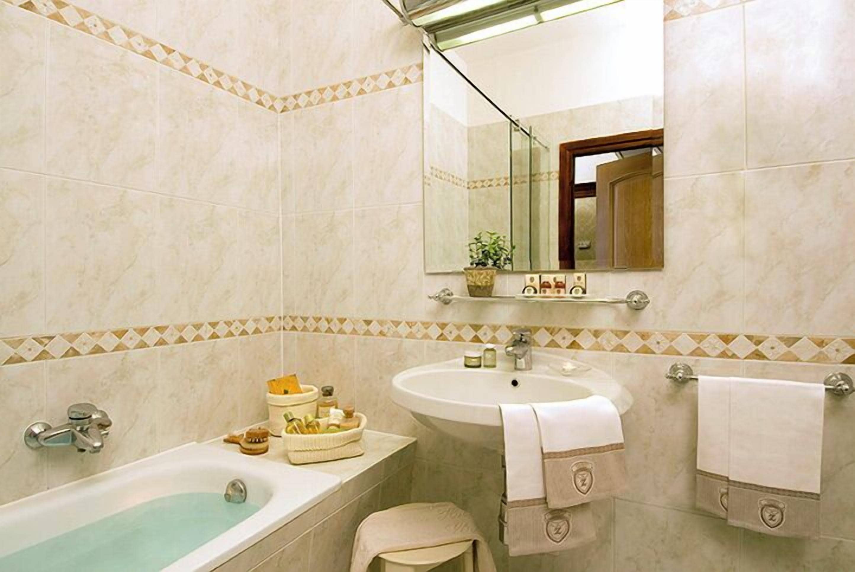 A bathroom with a bathtub, sink, and mirror. There are towels and toiletries on the sink counter.