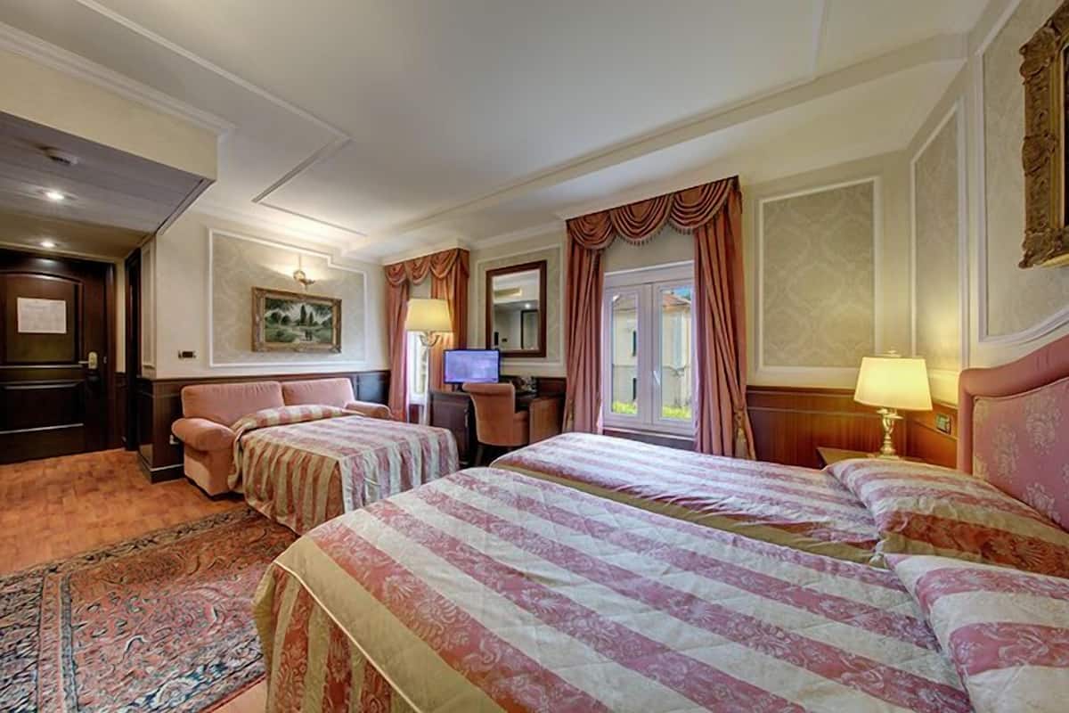 Quarto de hotel com duas camas, uma escrivaninha, uma televisão e uma janela grande com cortinas.