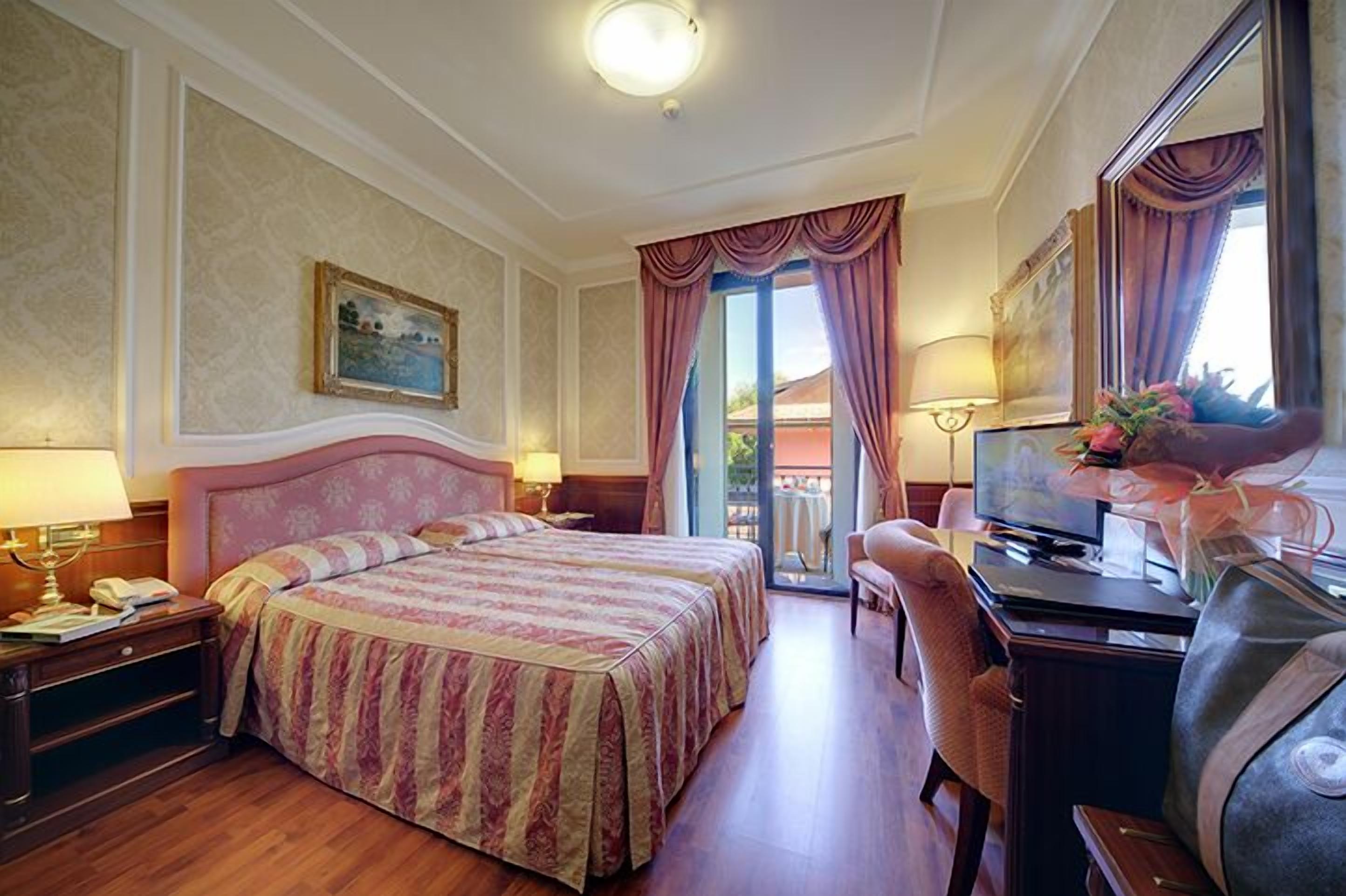 Habitación de hotel con una cama grande, un escritorio con computadora, una silla y un televisor.