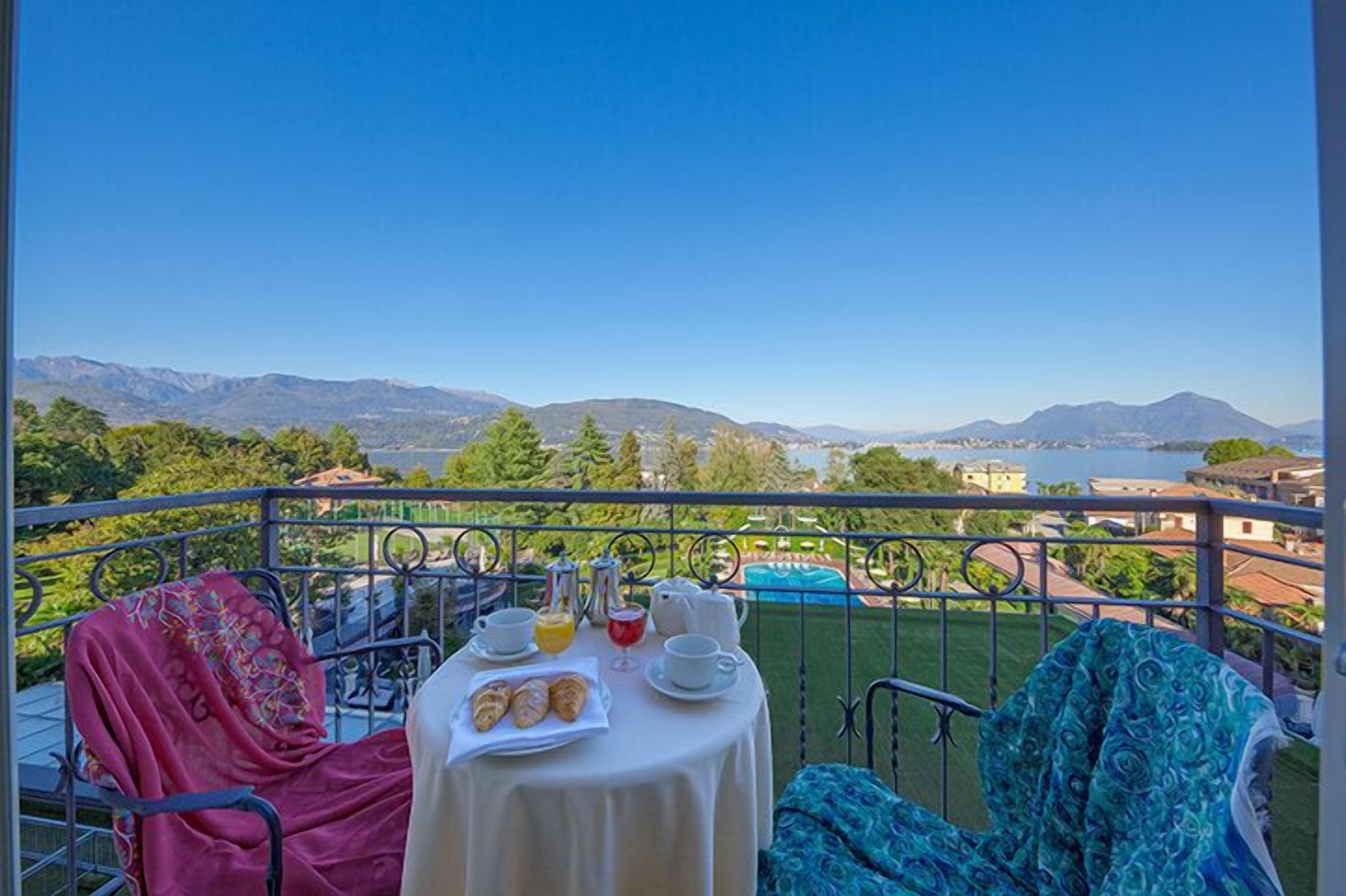 A balcony with a table set for breakfast, overlooking a scenic view of mountains and a body of water.