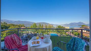 A balcony with a table set for breakfast, overlooking a scenic view of mountains and a body of water.