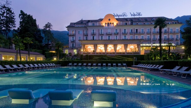 Un hotel con una piscina grande, tumbonas y una fachada bien iluminada.