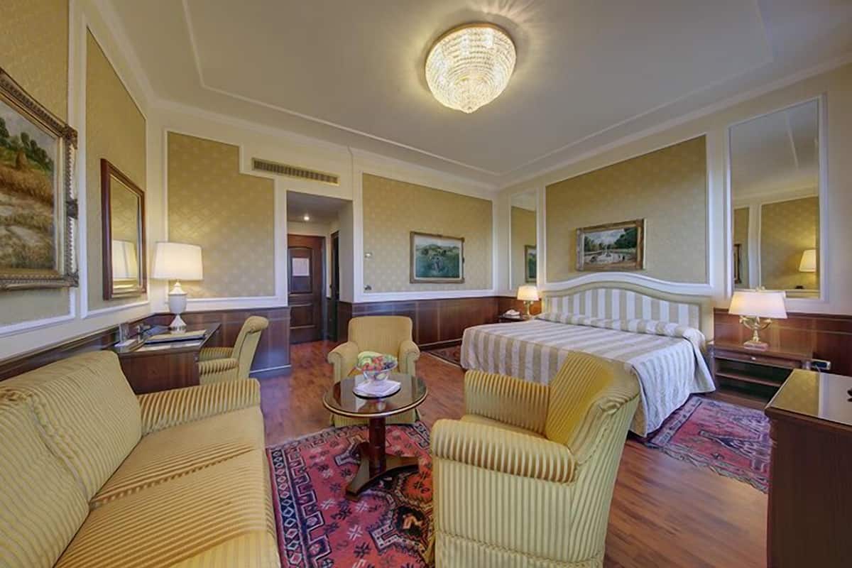 Quarto de hotel com cama, duas poltronas, um sofá, uma mesinha e um candelabro.