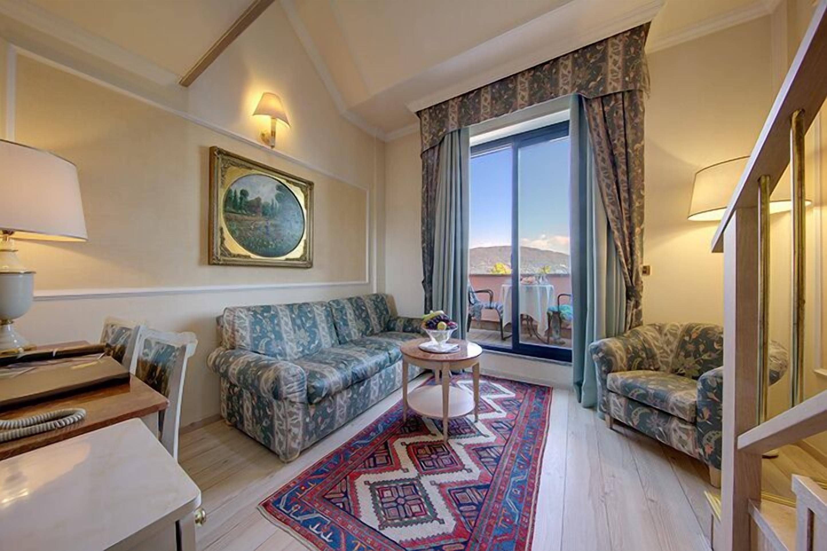 Un salon avec un canapé, une petite table sur laquelle se trouve un saladier rempli de fruits, un tapis à motifs et un tableau accroché au mur.
