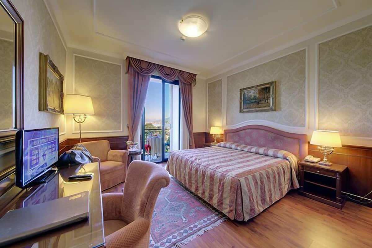 Quarto de hotel com uma cama, uma escrivaninha com computador, uma cadeira e uma televisão.