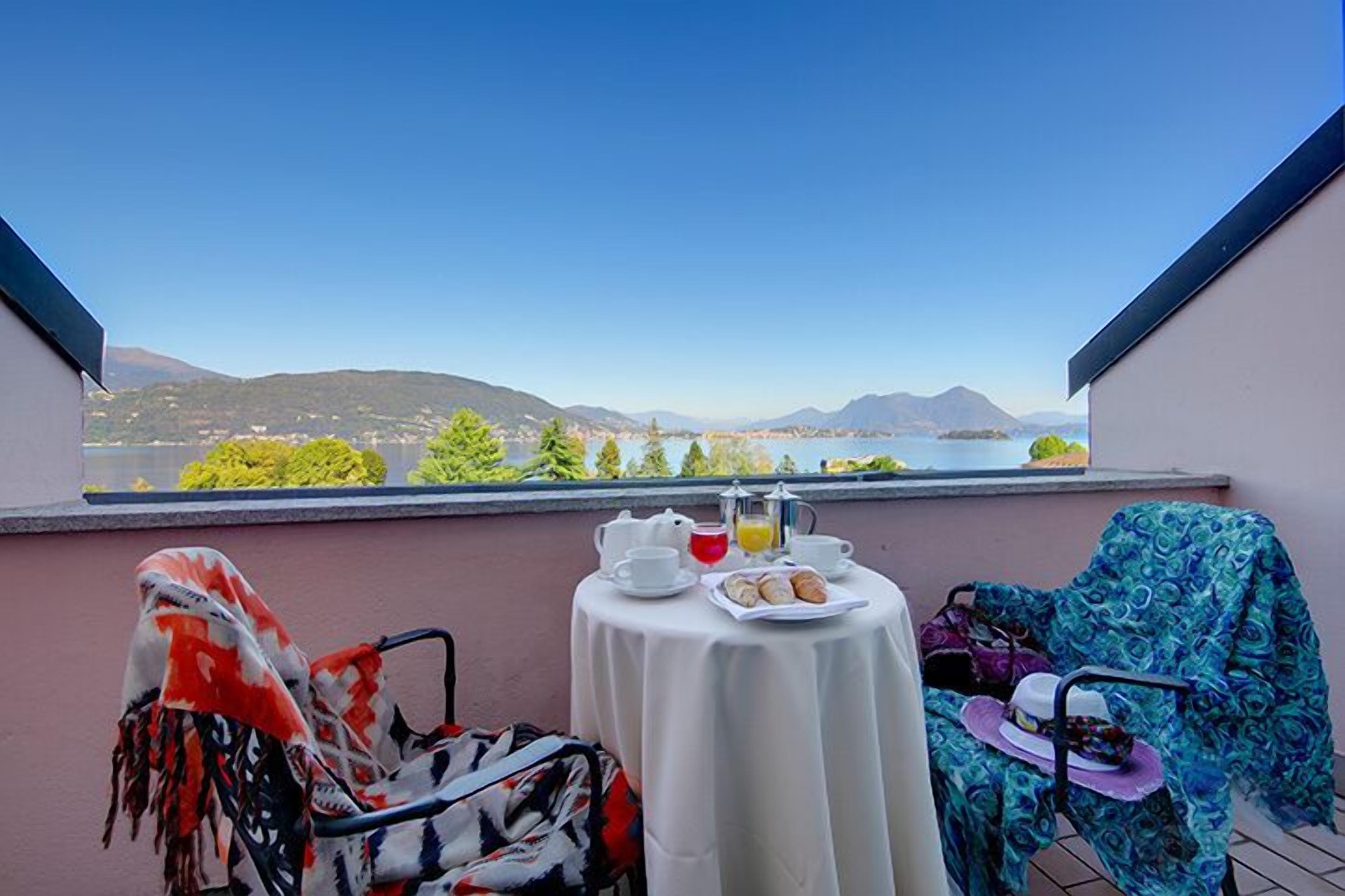 Ein Balkon mit Frühstückstisch, einem Stuhl und Blick auf einen See und Berge.