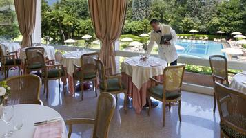 Restaurante con terraza al aire libre que da a una piscina, con sillas de mimbre y mesas redondas.