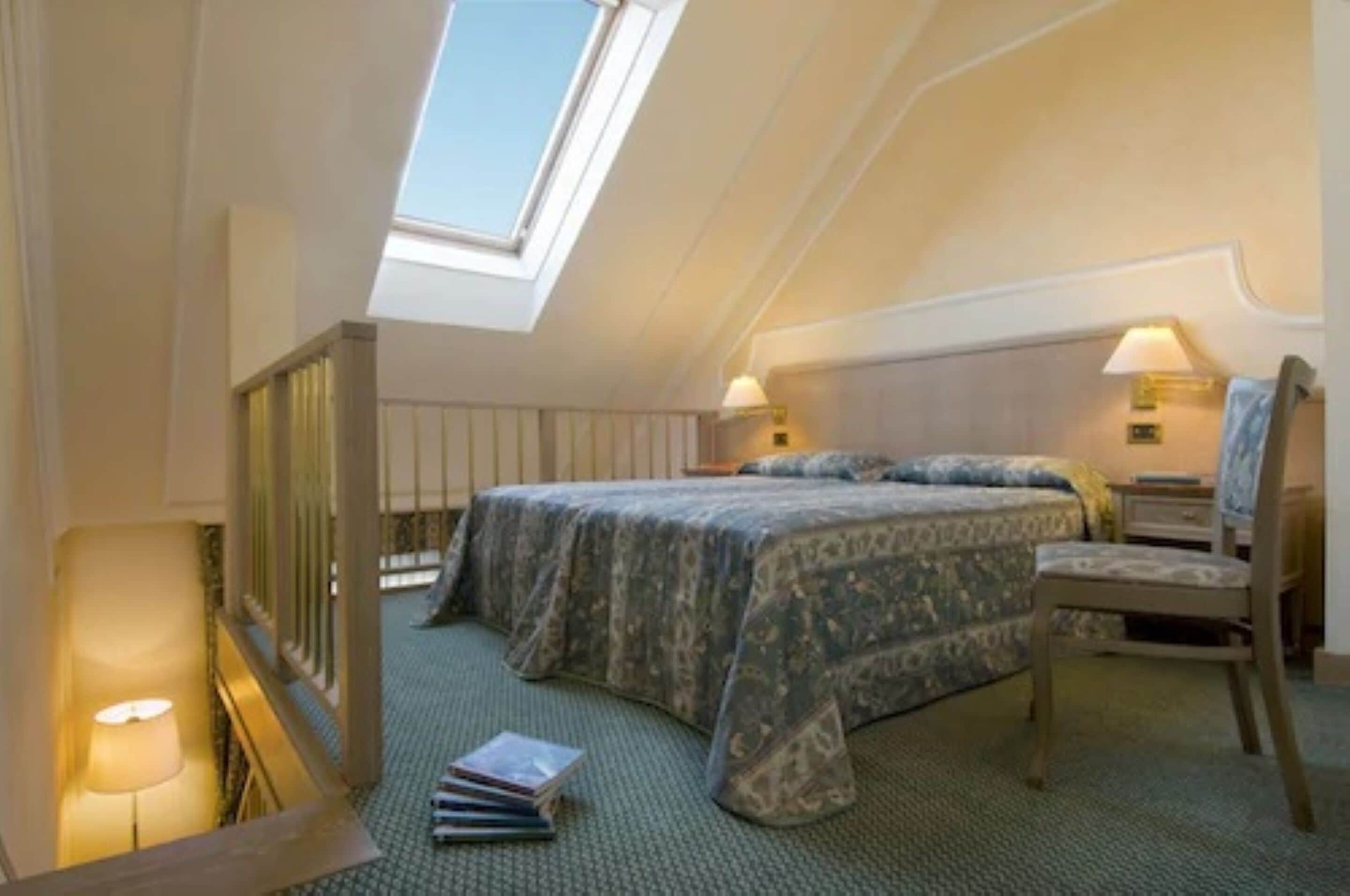 A bedroom with a skylight, a bed with patterned bedding, a chair, and bedside lamps.