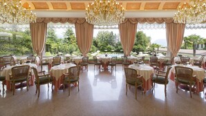 Un comedor formal con varias mesas y sillas, ventanas amplias con cortinas y un candelabro.