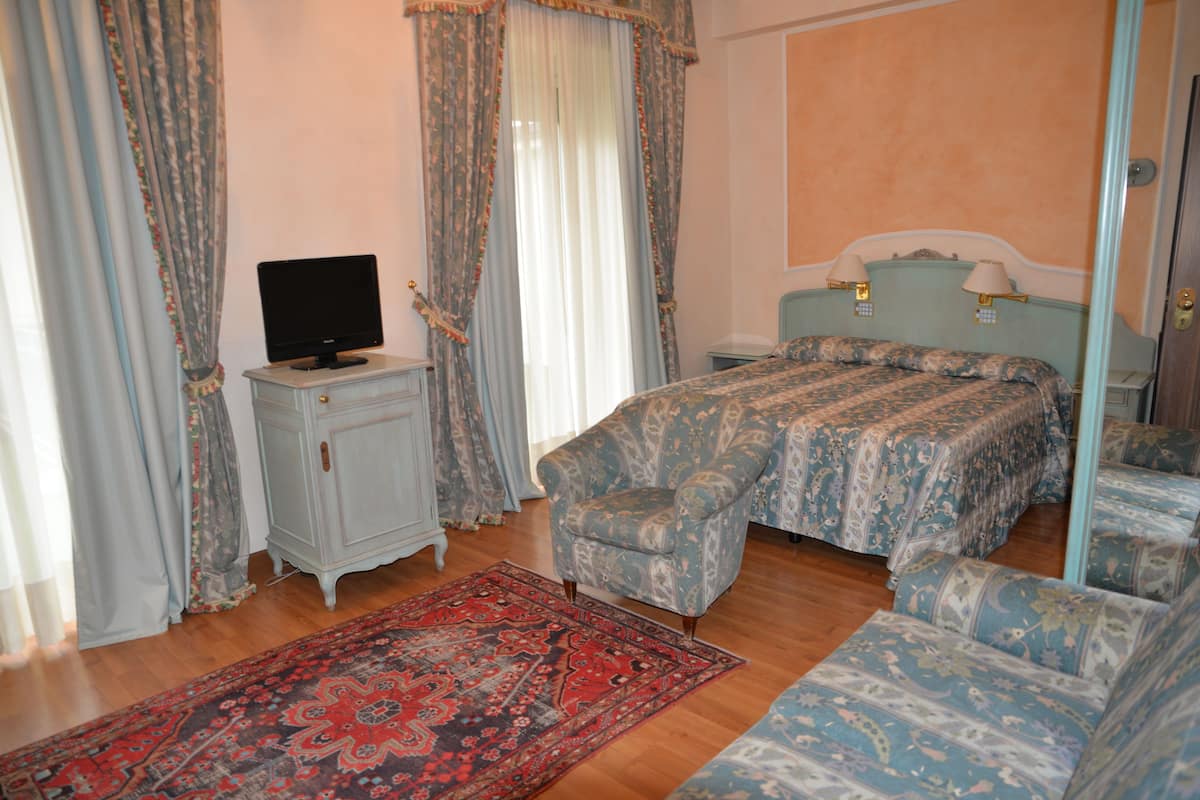 Quarto com cama, poltrona, televisão em cômoda e mesa de cabeceira com luminárias.