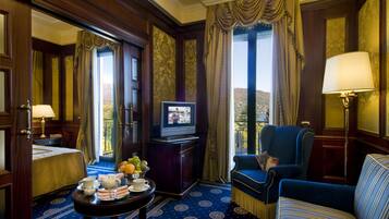 Habitación de hotel con un ventanal grande, televisor, una mesa de comedor con fruta y un sofá.
