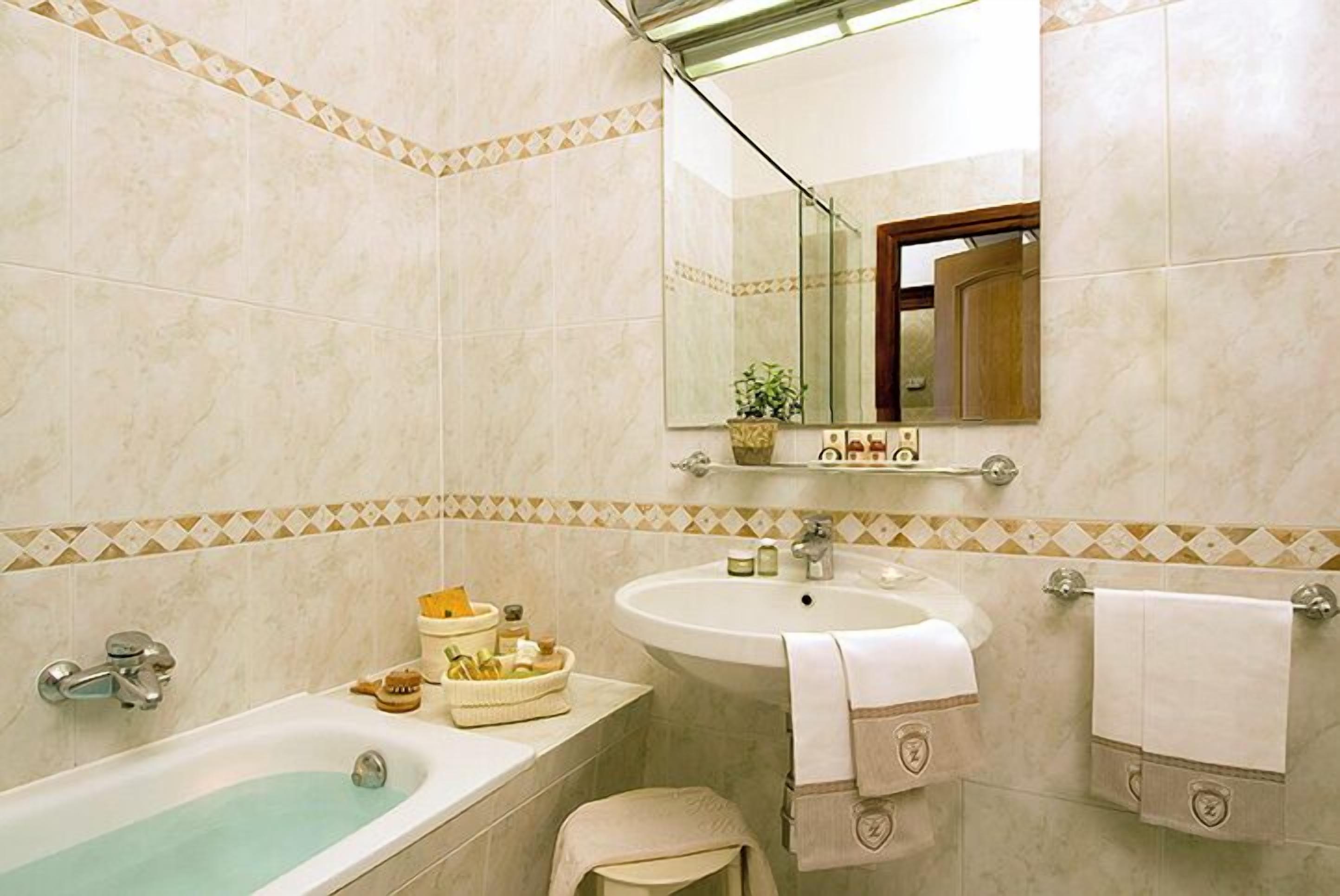 Een badkamer met een badkuip, wastafel en spiegel. Er liggen handdoeken en toiletartikelen op de wastafel.