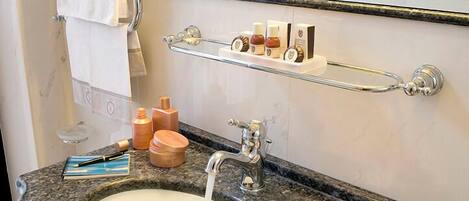 A bathroom with a granite sink, a towel rack with a white towel, a mirror, and toiletries on a shelf.