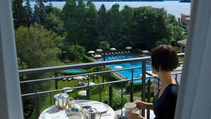 Un balcón con una mesa preparada para dos personas, con vista a una piscina y un lago con montañas al fondo.