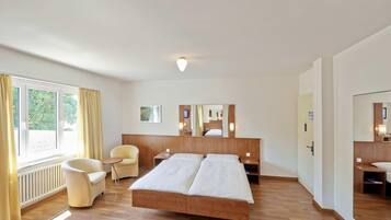 Ett hotellrum med en dubbelsäng, ett litet bord, två stolar, ett fönster med gardiner, ett element och en spegel på väggen.