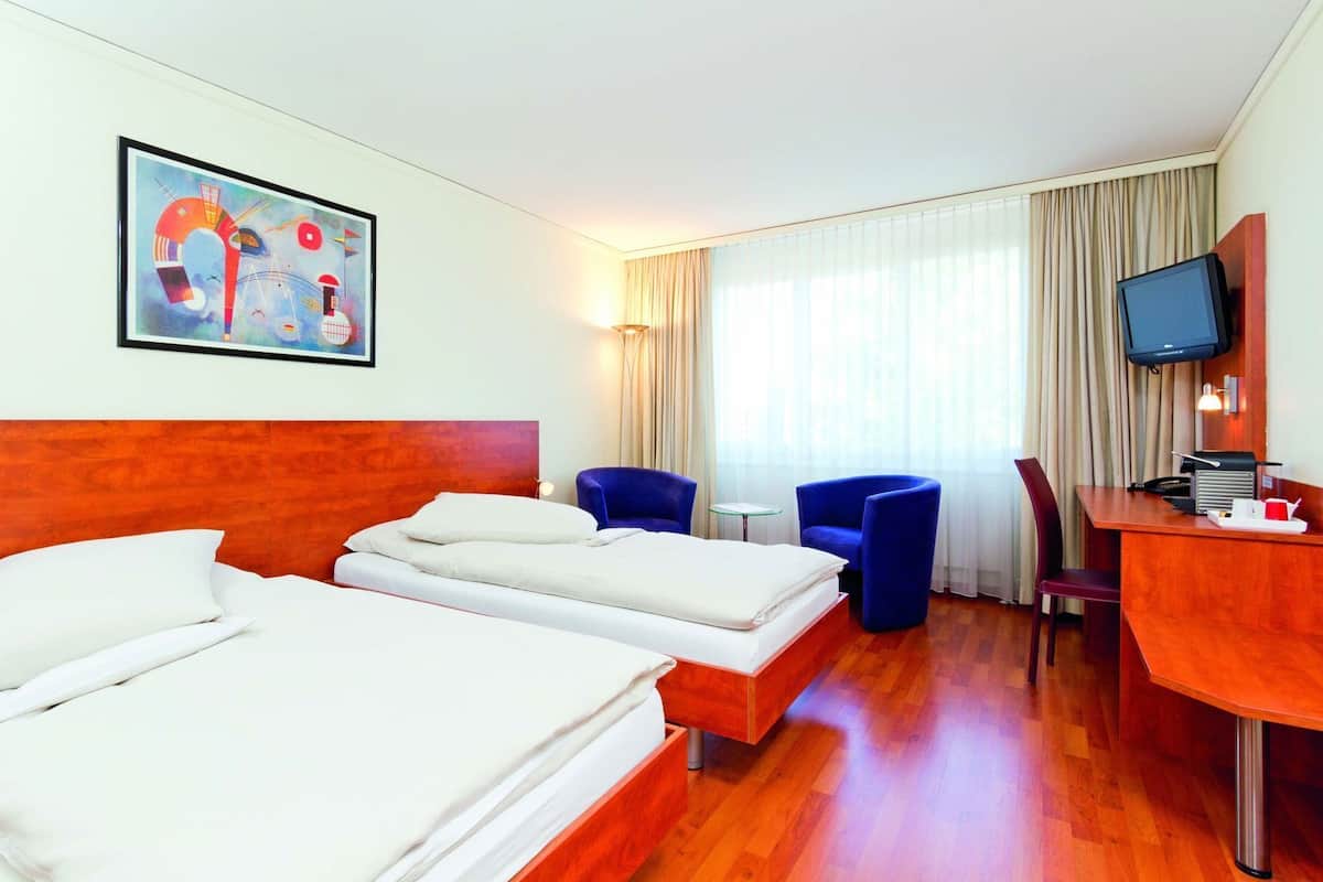 Una habitación de hotel con dos camas, un escritorio, un televisor y un cuadro en la pared.