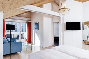 Una habitación de hotel moderna con una cama grande, un sofá, un televisor y una araña.
