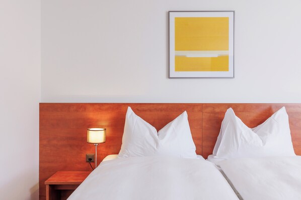 A hotel room with a wooden headboard, white bedding, a bedside lamp, and a framed abstract artwork on the wall.