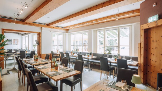 Un restaurante con vigas de madera, ventanas amplias y mesas dispuestas para comer.