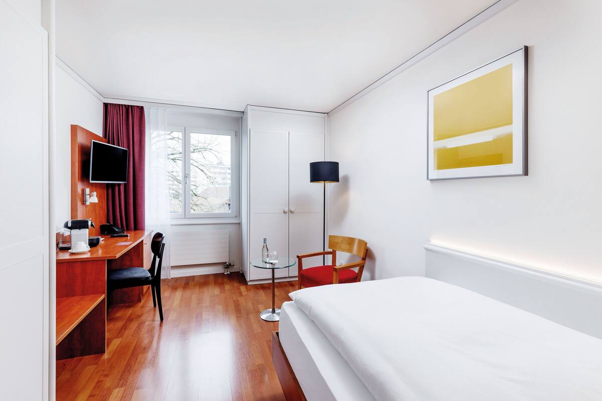 Habitación de hotel con cama, escritorio, silla, televisión, lámpara y obras de arte.