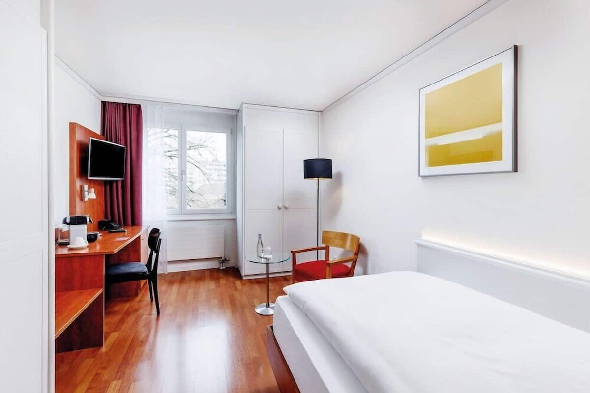 Habitación de hotel con cama, escritorio, silla, televisión, lámpara y obras de arte.